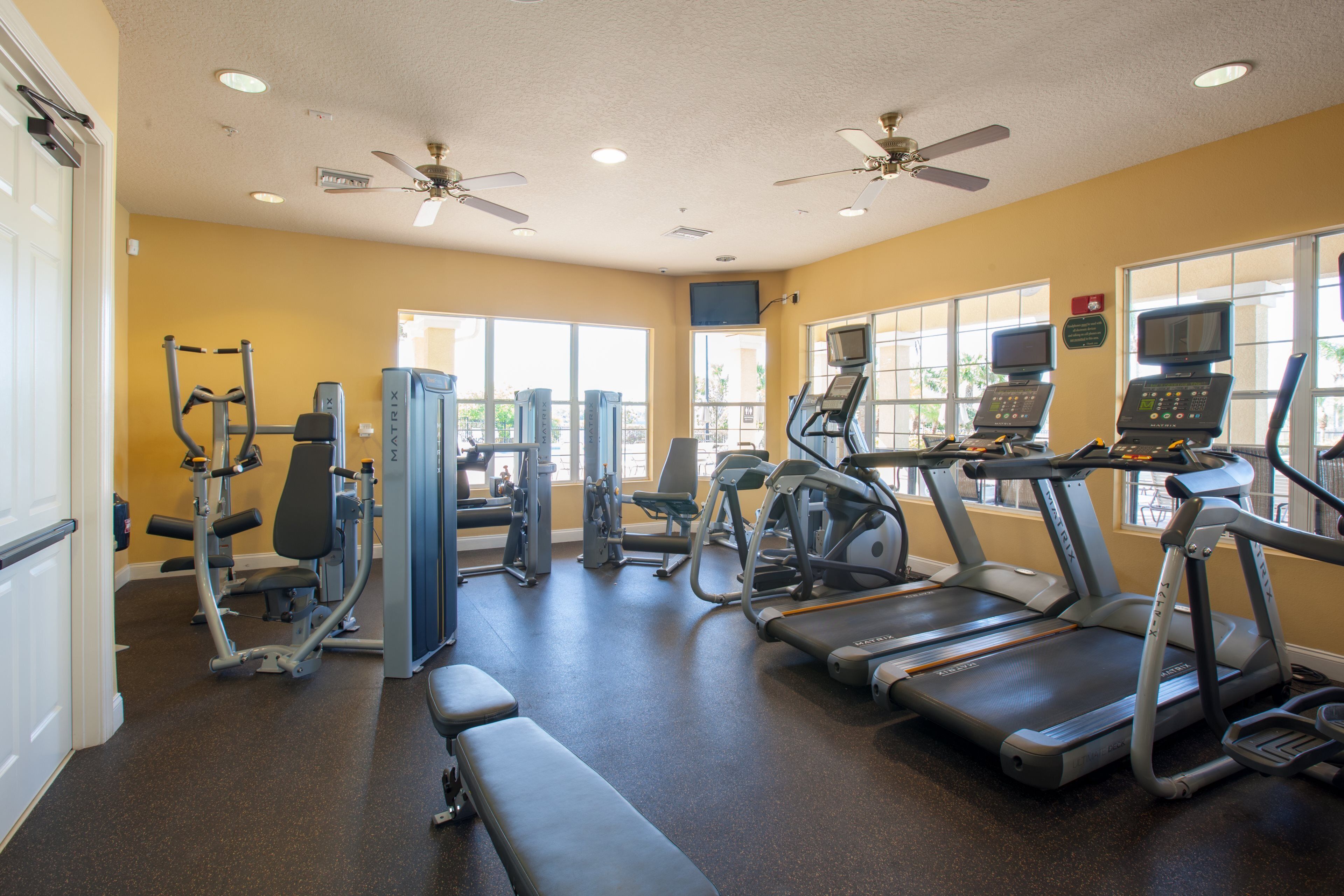 Une salle de sport équipée de tapis de course, d’appareils de musculation et d’un banc.