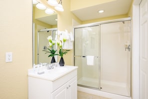 Un baño con tocador blanco, cabina de ducha con mampara de vidrio y espejo con iluminación.