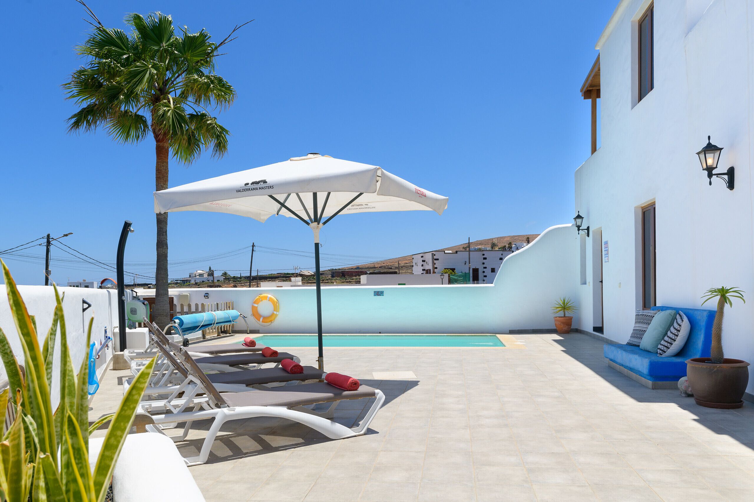 A poolside area with lounge chairs, a white umbrella, and a blue sofa.