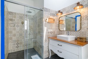 A bathroom with patterned tiles, a glass shower enclosure, a white vanity with a wooden countertop, and a mirror with wall-mounted lights. - Apartment Blue, Casa El Patio (Adults Only) (Teguise (Lanzarote))