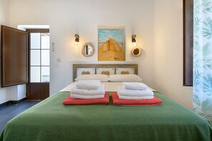 A hotel room with a bed, green bedspread, two red towels, a painting above the bed, and a window with a view. - Apartment Blue, Casa El Patio (Adults Only) (Teguise (Lanzarote))