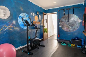 Ein Fitnessraum mit Trainingsgeräten, einer Wandmalerei und einer Tür zu einem weiteren Raum.