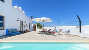 A poolside area with lounge chairs, a white umbrella, and a blue sofa. - Apartment Blue, Casa El Patio (Adults Only) (Teguise (Lanzarote))