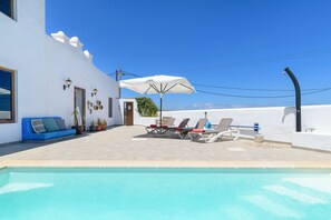 A pool area with lounge chairs and an umbrella, a white building with a door and windows, and a clear blue sky. - Apartment Blue, Casa El Patio (Adults Only) (Teguise (Lanzarote))