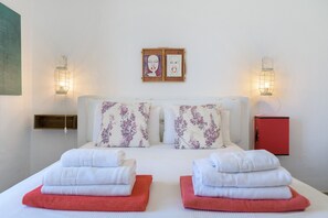 A neatly made bed with floral pillows, two wall-mounted light fixtures, and a small red cabinet. - Apartment Green, Casa El Patio (Only Adults) (Teguise (Lanzarote))