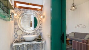 Un baño con un lavabo blanco, baldosas azules con diseño, un espejo redondo y una puerta verde.