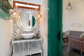 A bathroom with a white sink, blue patterned tiles, a round mirror, and a green door.