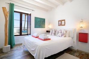 A bedroom with a bed, a window with curtains, a painting, wall-mounted lights, and a red cabinet.