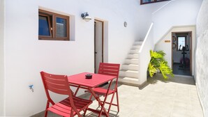 Un pequeño patio con una mesa y sillas rojas, una escalera y una planta en maceta.