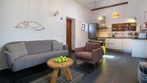 A modern living room with a grey sofa, a striped armchair, and a small wooden table with apples. A kitchen is visible in the background with a wooden cabinet and a hanging light fixture. - Apartment Green, Casa El Patio (Only Adults) (Teguise (Lanzarote))