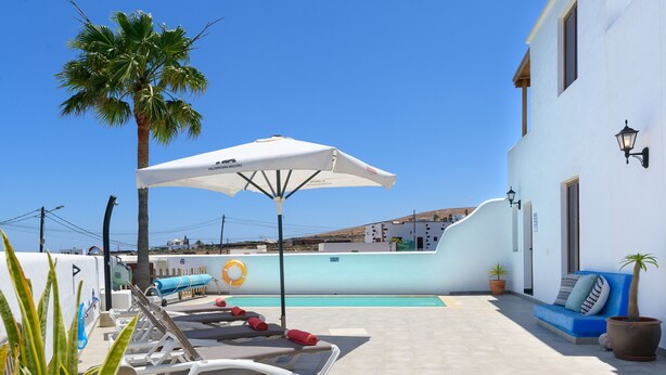 A poolside area with lounge chairs, a white umbrella, and a blue sofa. - Apartment Green, Casa El Patio (Only Adults) (Teguise (Lanzarote))