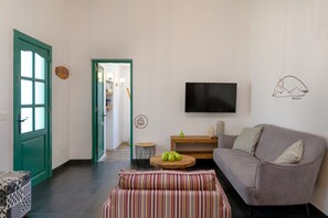 Een woonkamer met een groene deur, een bank, een televisie en een muur met een bergtekening.