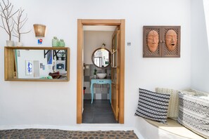 A hallway with a wooden door leading to a bathroom with a sink and mirror. There are decorative items on the wall and a sofa with patterned cushions. - Apartment Green, Casa El Patio (Only Adults) (Teguise (Lanzarote))