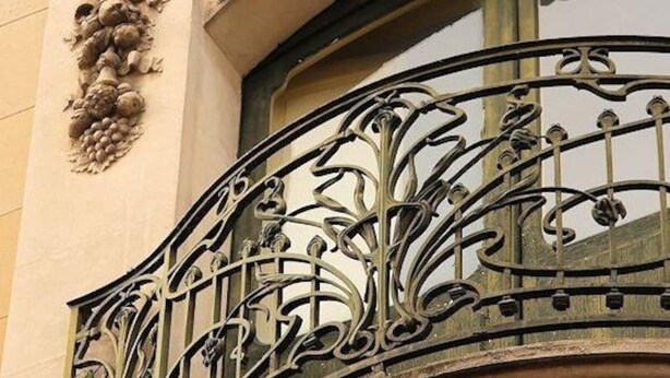 Een gevel met versierde stenen beeldhouwwerken en een balkon van ijzerwerk.
