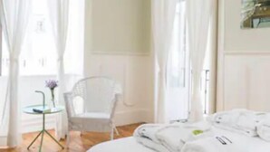 Ein Hotelzimmer mit einem großen Bett, weißen Vorhängen, einem kleinen Tisch mit einer Vase und einem Sessel.