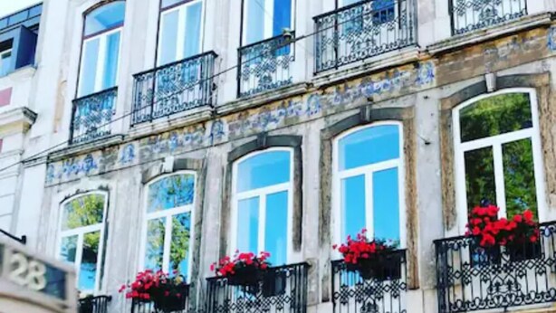 Ein historisches Gebäude mit mehreren Balkonen, großen Fenstern und roten Blumen in den Fensterkästen.