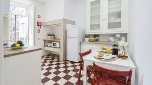 Eine moderne Küche mit Schachbrettmuster-Boden, weißen Schränken, einem Kühlschrank, einer Mikrowelle und einem Essbereich mit roten Stühlen.