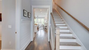 A hallway with a wooden staircase leading to a bright room with a kitchen area. - Current Situation| 4 Bdrm w/ 3 Kings | Heated Pool | Golf Cart (Santa Rosa Beach)