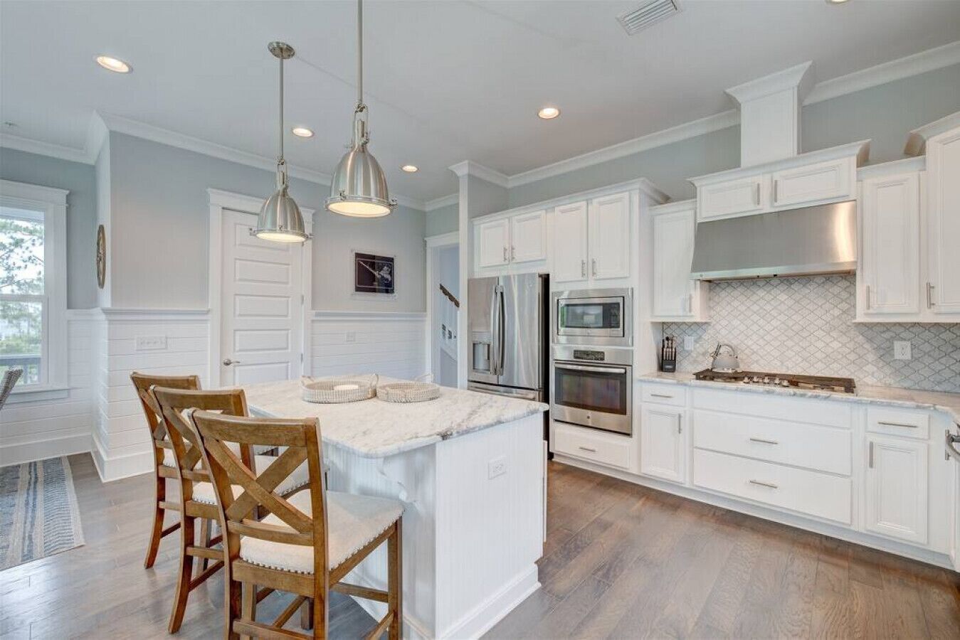 A spacious kitchen with white cabinetry, a large island with chairs, stainless steel appliances, and pendant lighting.