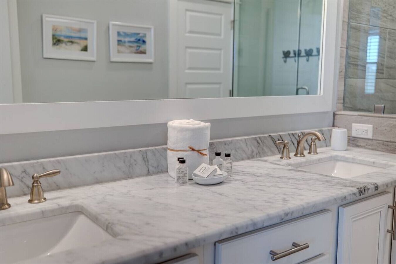 A bathroom with marble countertops, two sinks, gold faucets, and a large mirror.