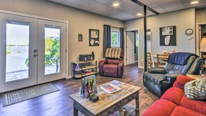 A spacious living room with a fireplace, leather recliners, a coffee table with magazines, and a view of the outdoors through large windows. - Hidden Gem: Dock & Views on Pine Hollow Reservoir! (Tygh Valley)