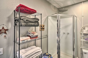 Un baño con cabina de ducha de vidrio, un perchero metálico con toallas dobladas y un cartel en la pared.