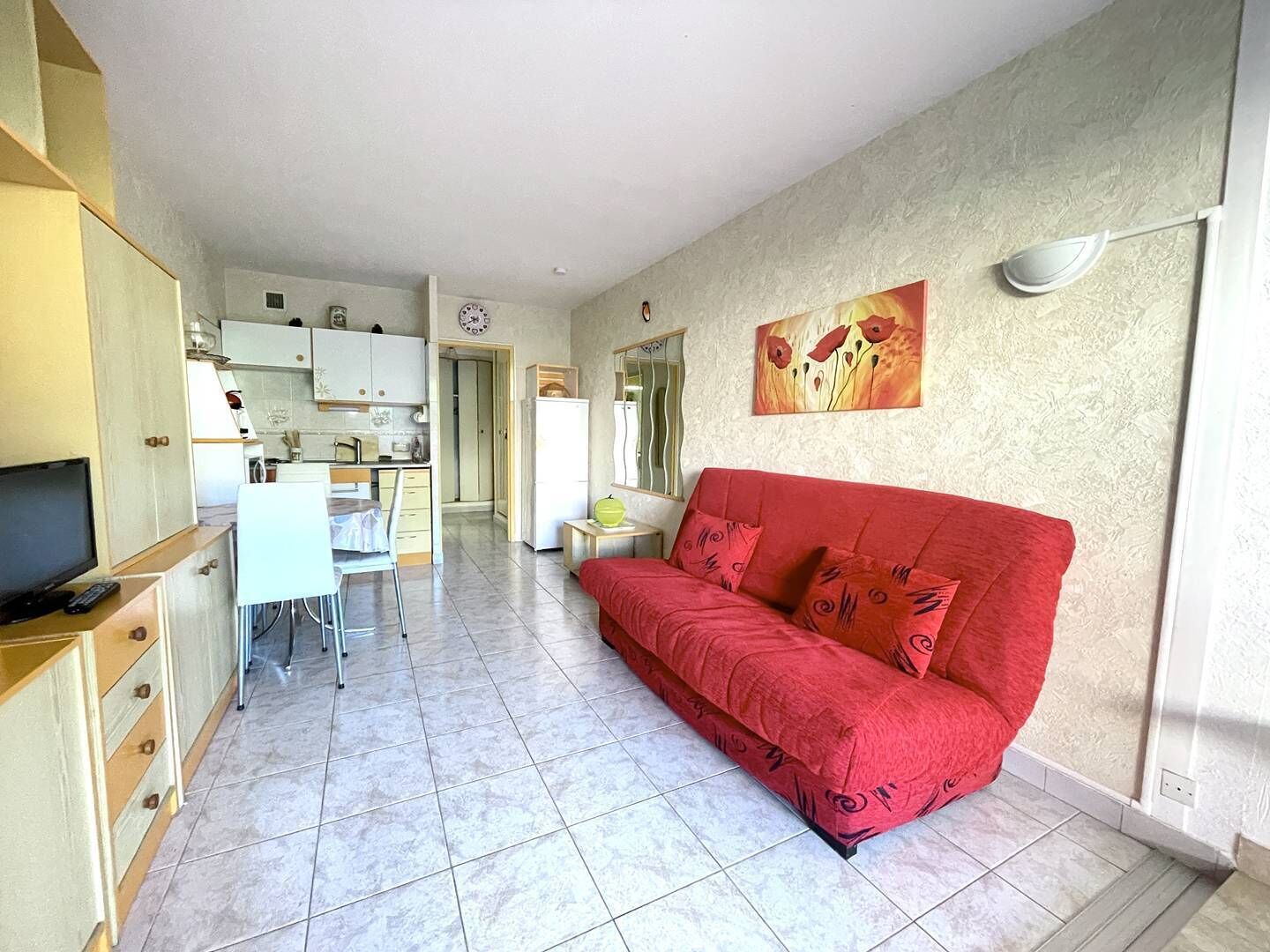 Een ruimtelijk ingerichte leefruimte met een kitchenette, een rode bank en een eethoek.