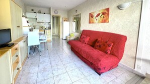 A compact living space with a kitchenette, a red sofa, and a dining area. - AGREABLE STUDIO EN REZ DE JARDIN AVEC GRANDE TERRASSE (LE CAP D AGDE)