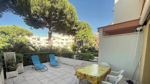 A patio with a table and chairs, a large tree, and a building in the background. - AGREABLE STUDIO EN REZ DE JARDIN AVEC GRANDE TERRASSE (LE CAP D AGDE)