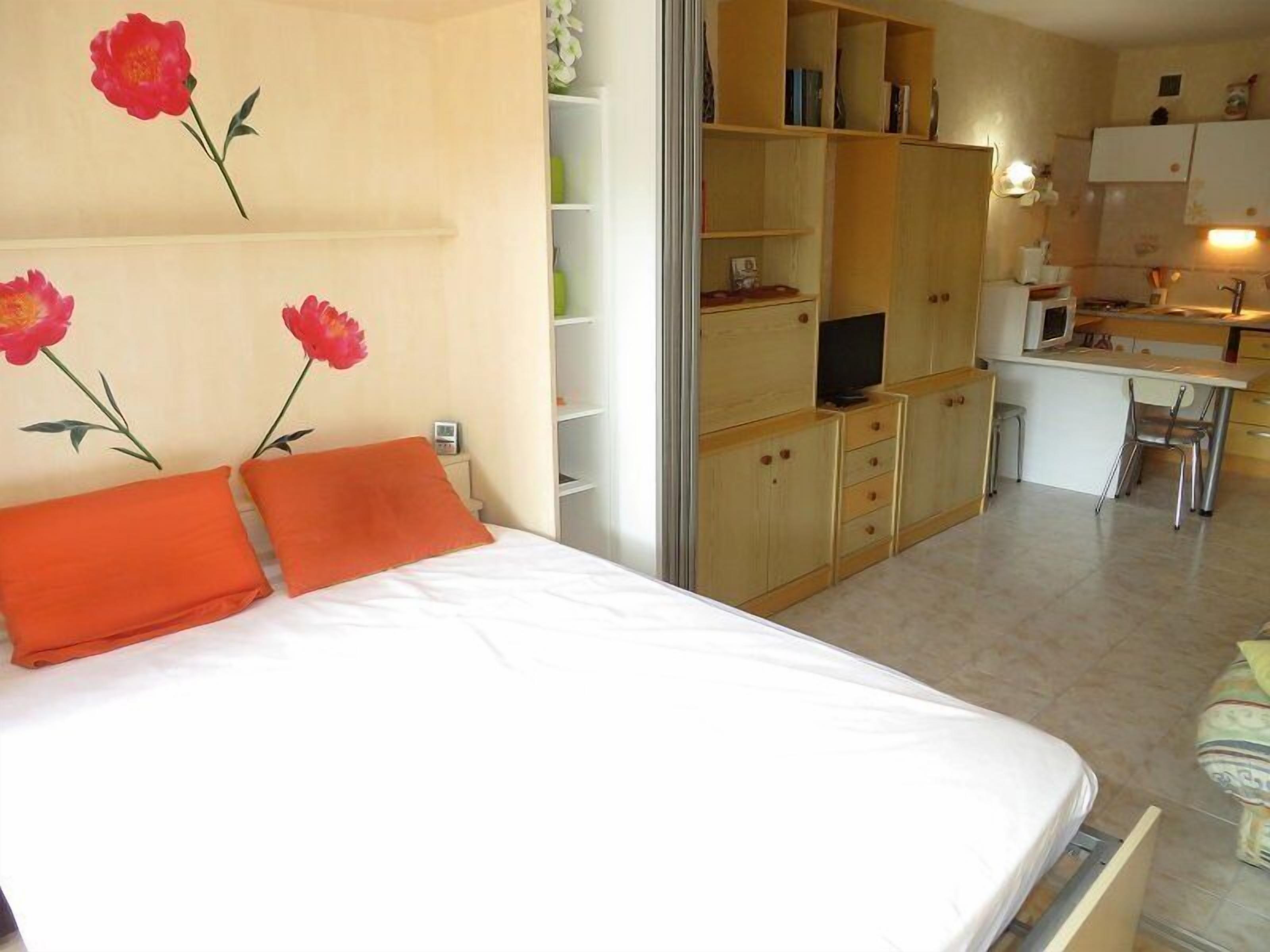 A bedroom with a bed, orange pillows, a desk, a chair, and a TV.