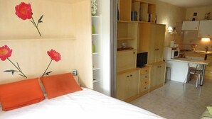 A bedroom with a bed, orange pillows, a desk, a chair, and a TV. - AGREABLE STUDIO EN REZ DE JARDIN AVEC GRANDE TERRASSE (LE CAP D AGDE)