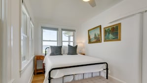 Un dormitorio con cama, un banco, una mesita de noche y dos cuadros en la pared.