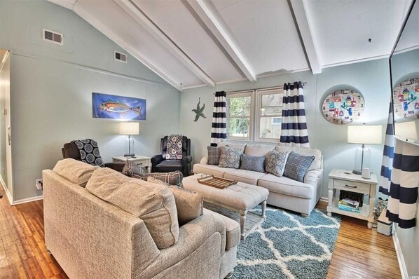 A living room with a sofa, armchair, and a coffee table. There are two lamps, a clock, and a starfish decoration on the wall.