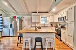 A modern kitchen with white cabinets, a wooden island, and stainless steel appliances.