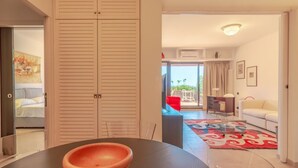 Ein modernes Wohnzimmer mit Essbereich, einer Couch, einem roten Sessel und Blick ins Freie.