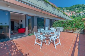 A patio with a round table and chairs, a red sofa, and a glass door leading to an interior space. - CASA CARLOTTA - Peaceful with a Sea View (Camogli)