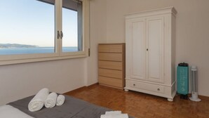 A bedroom with a large window, a wardrobe, a bed with rolled towels, and a standing fan. - CASA LINDA - Dream view, swimming pool, and tennis court (Rapallo)
