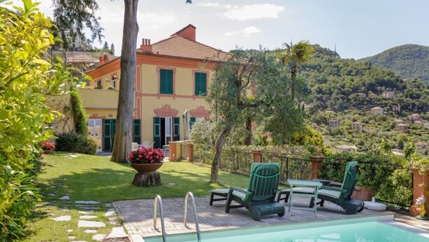 A pool with lounge chairs, a stone pathway, and a view of a hillside town. - VILLA AURORA - Relax with Sea View and Swimming Pool (Camogli)