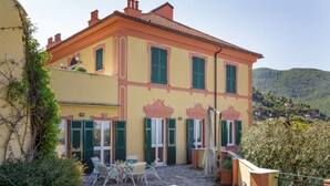 A two-story building with a stone patio, green shutters, and a view of a hillside. - VILLA AURORA - Relax with Sea View and Swimming Pool (Camogli)