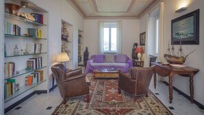 A room with a sofa, chairs, a bookshelf, a table with a ship model, and a window. - VILLA AURORA - Relax with Sea View and Swimming Pool (Camogli)
