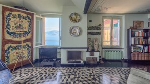 Un salon avec un grand tableau, une cheminée, une bibliothèque et une vue sur la mer.