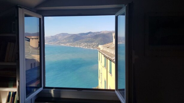Une pièce dotée d’une grande fenêtre donnant sur une ville côtière et des montagnes.