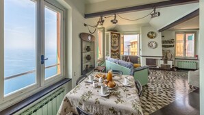 Une pièce avec une table à manger dressée pour le petit-déjeuner, une vue sur la mer à travers de grandes fenêtres et un sol à motifs.