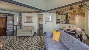 Un salon avec un tapis à motifs, un canapé, un fauteuil et un coin repas comprenant une table et des chaises.
