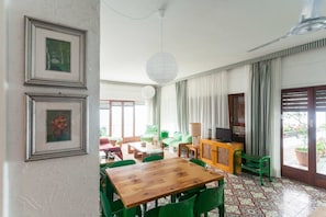 A room with a wooden table, green chairs, a sofa, a TV, and curtains.