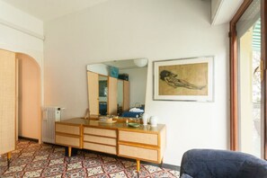 A room with a wooden dresser, a large mirror, a framed painting, and patterned floor tiles.