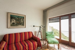 A room with a striped sofa, a chair, a telescope, and a balcony with a view.