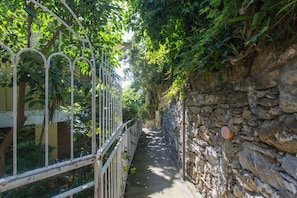 A narrow stone pathway flanked by metal railings and lush greenery.