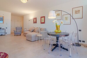 Una sala de estar moderna con una mesa de comedor redonda, sillas traslúcidas, un sofá, una silla y una lámpara de pie.