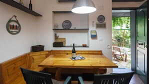 Una mesa de comedor de madera con una botella y vasos, una lámpara colgante y estantes con objetos decorativos.